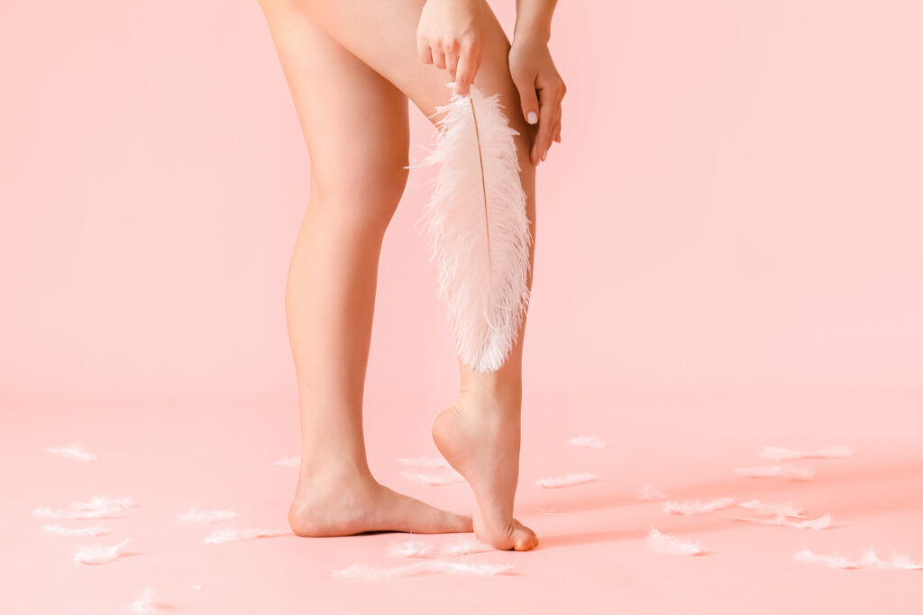 Legs of young woman with soft feather on color background. Epilation concept